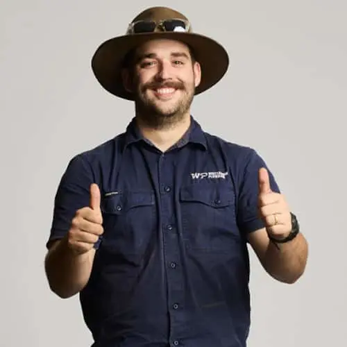 Person in navy work shirt and brown hat giving thumbs up against light background