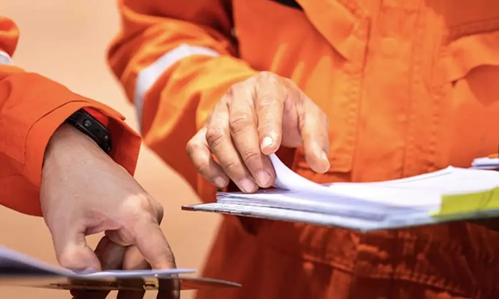 Person in bright orange safety uniform reviewing documents on a clipboard, with hands visible examining paperwork.