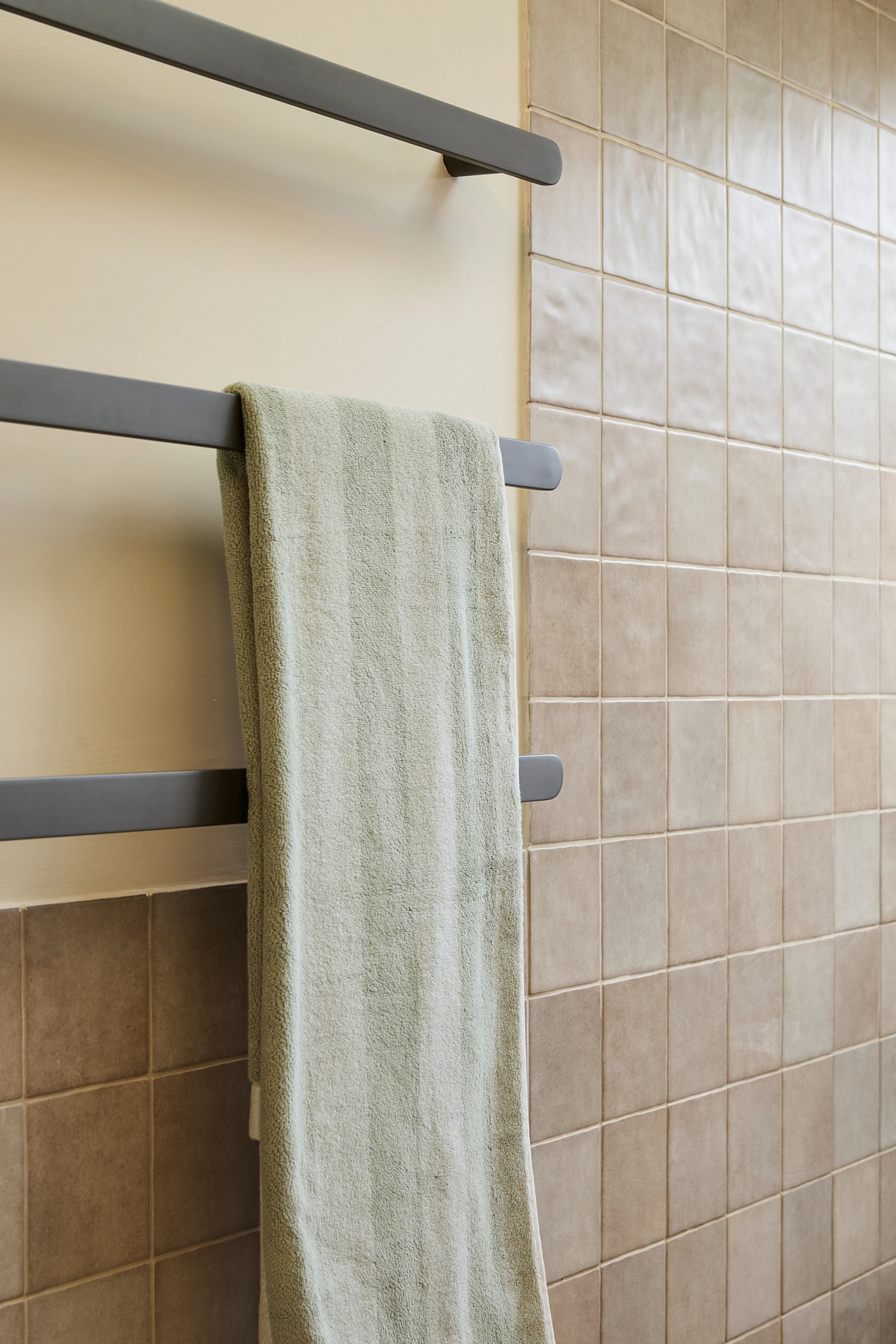 Modern gray towel rack with light green towel mounted on beige wall with square tile in bathroom.