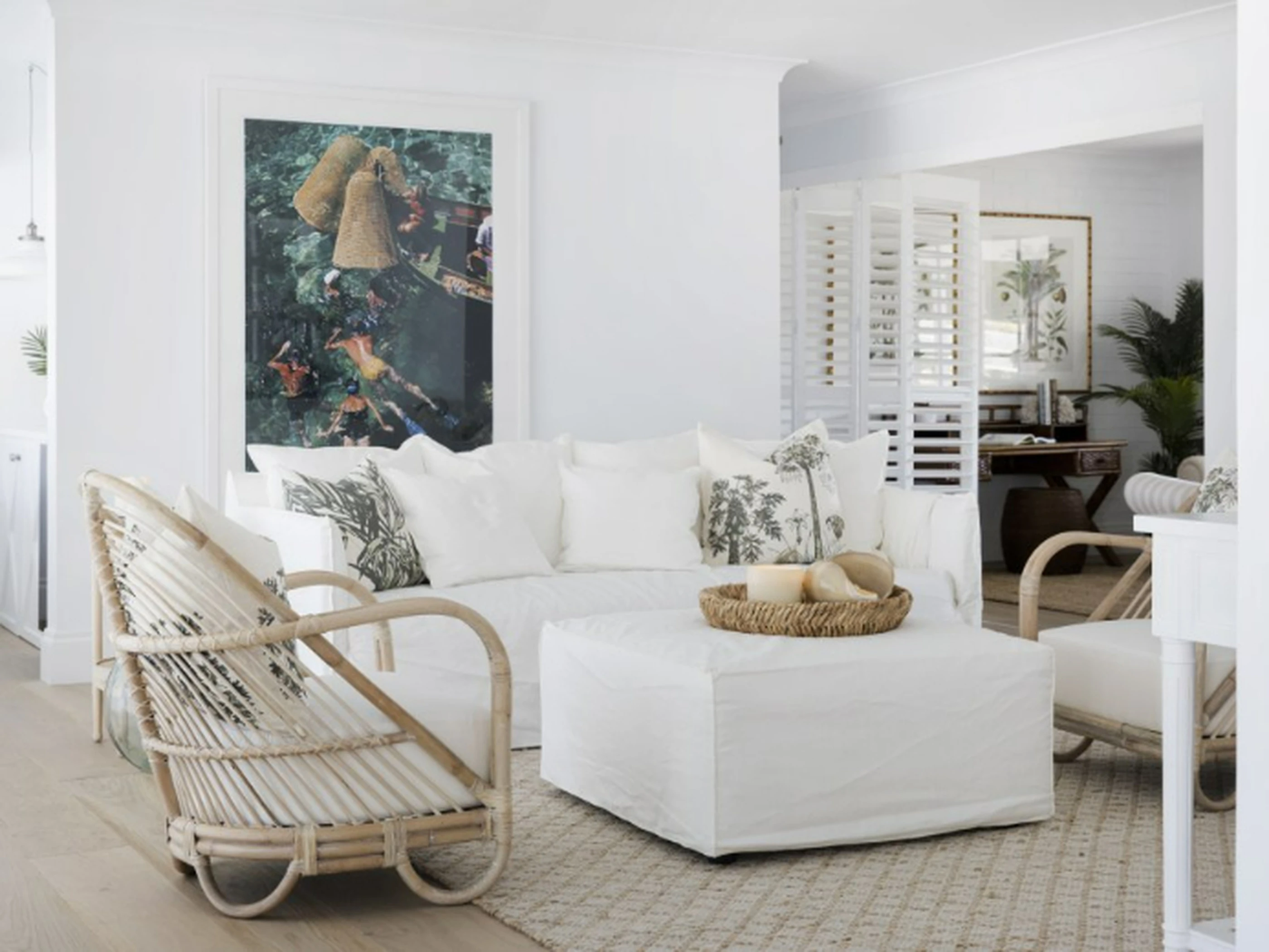 Bright coastal living room with white sofa, rattan chair, colorful wall art, and natural accents on a neutral area rug.