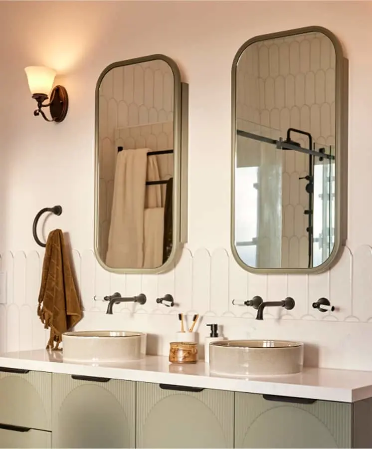 Elegant bathroom with dual sinks, arched mirrors, white tile backsplash, and black fixtures on a light green vanity.