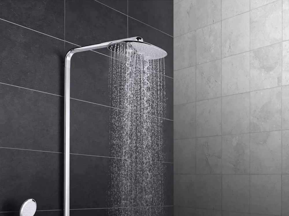 Modern shower system with rainfall showerhead spraying water against contrasting dark and light tiled bathroom walls.