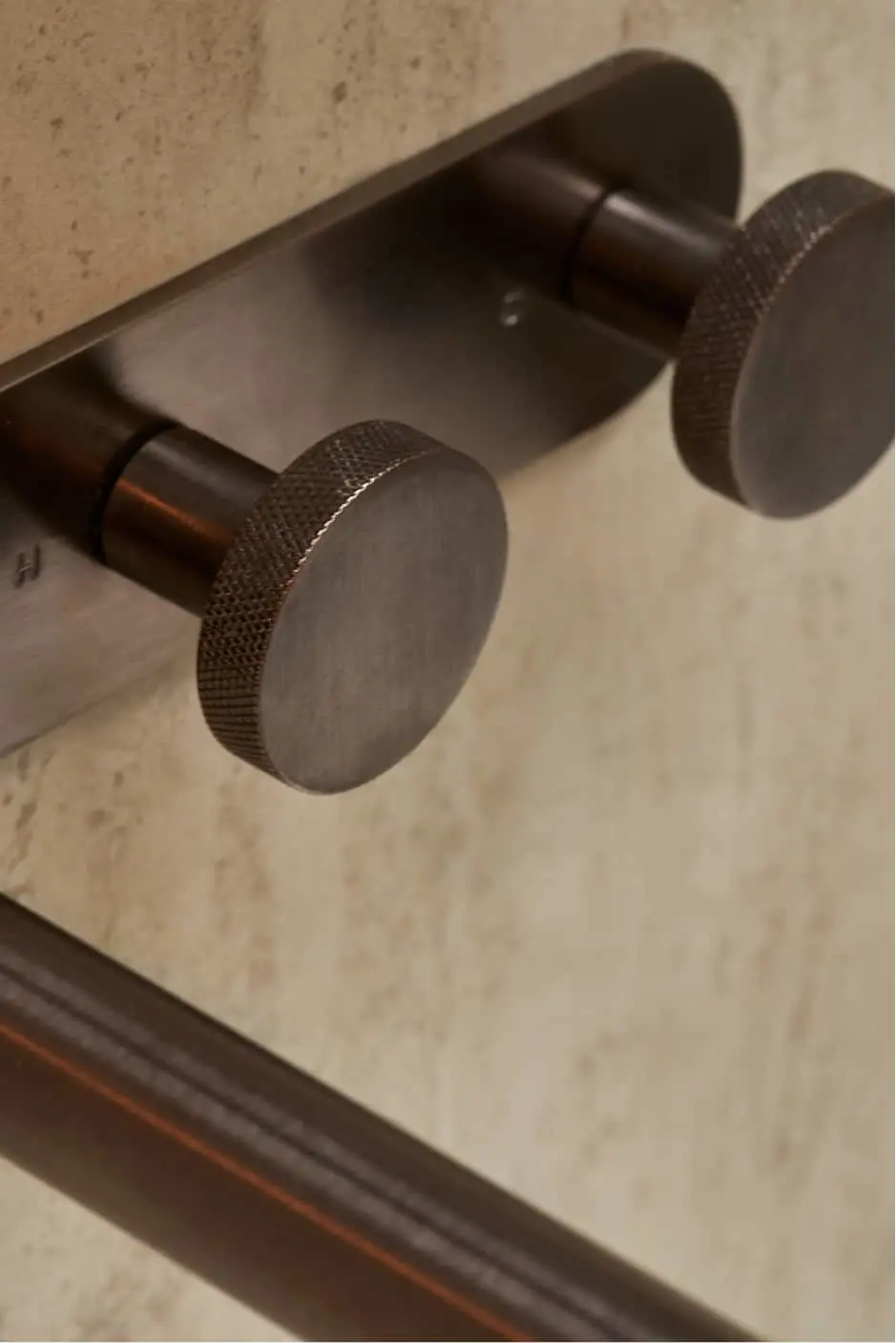 Close up of dark bronze basin mixers with cylindrical knobs mounted on a light-colored surface.