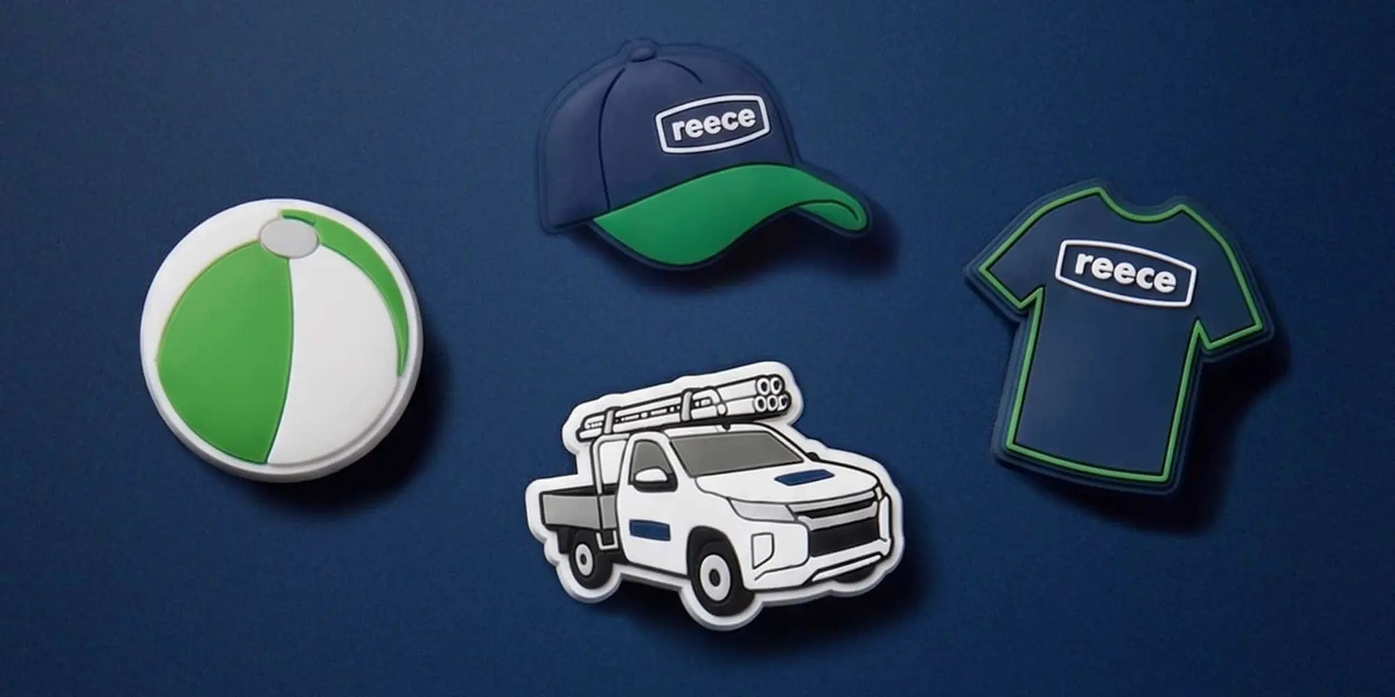 Four rubber Croc charms on a navy background: a green and white ball, a Reece cap, a ute, and a Reece t-shirt.