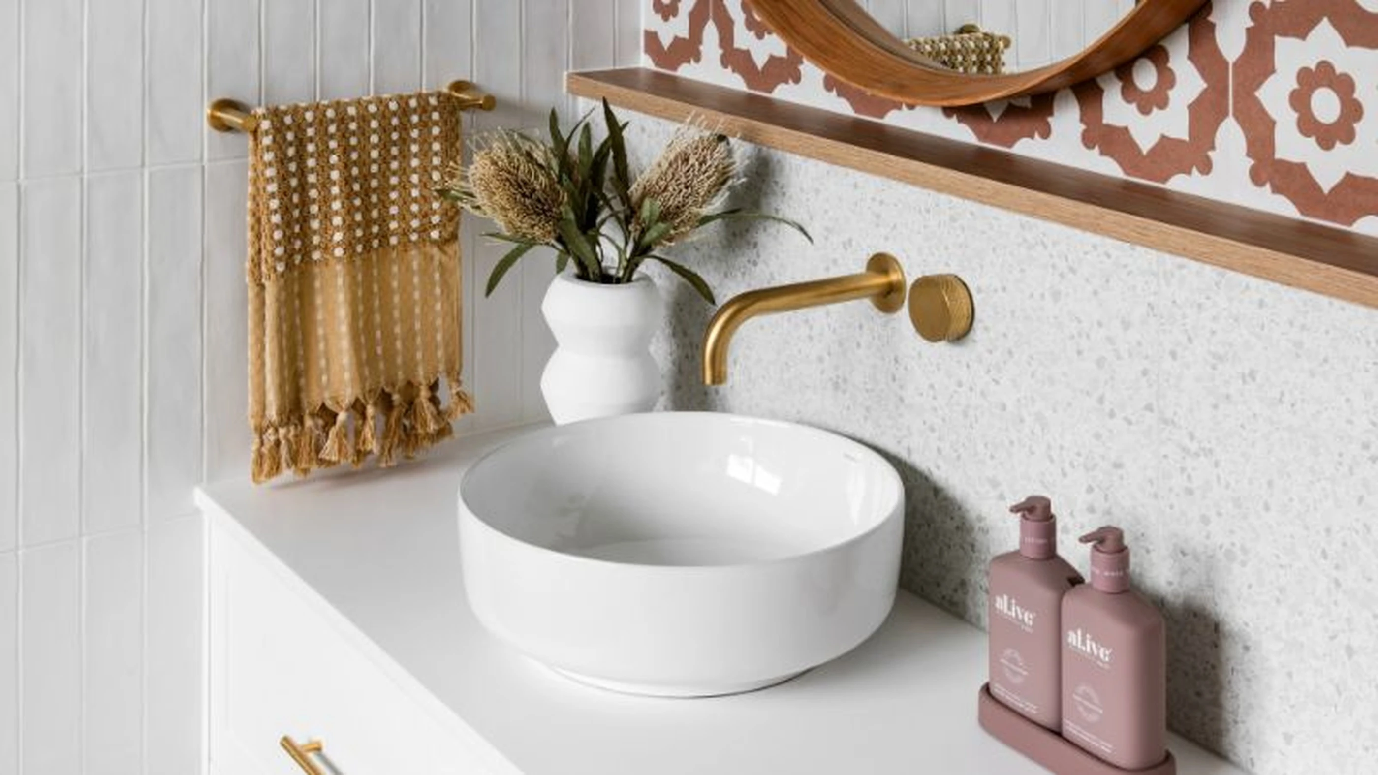Modern bathroom with white vessel sink, brass faucet, patterned tiles, and decorative elements in gold and pink tones.