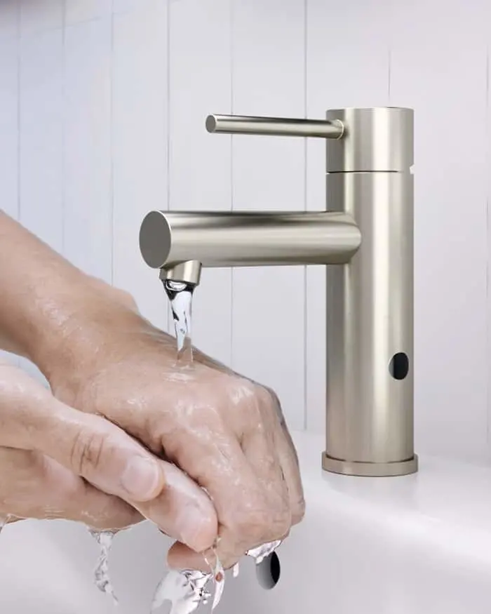 Person washing hands under a modern brushed stainless steel bathroom faucet with water running.