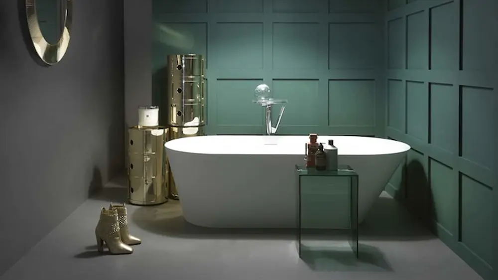 Modern bathroom with white freestanding tub, teal paneled walls, gold metallic storage unit, and stylish boots on floor.