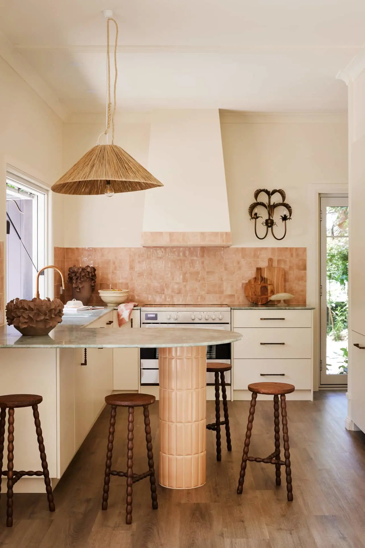 Modern kitchen with cream cabinets, peach tile backsplash, woven pendant light, and wooden barstools around a circular island.