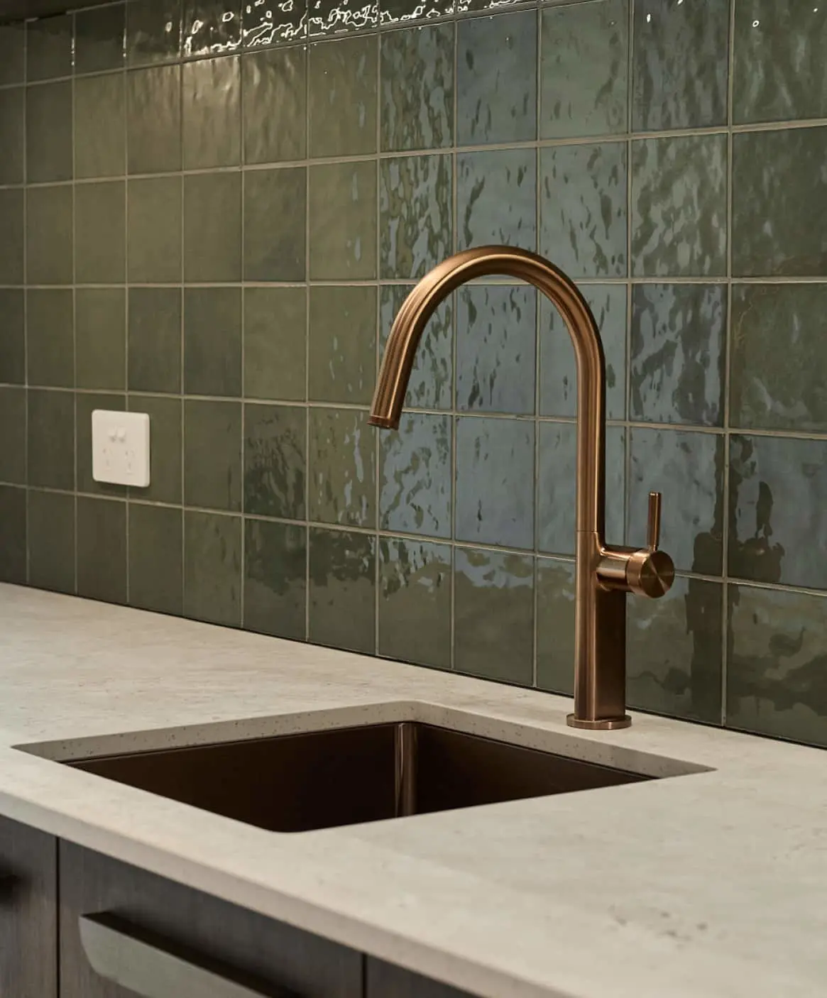 Modern kitchen sink with copper faucet, white countertop, and green glossy tile backsplash.