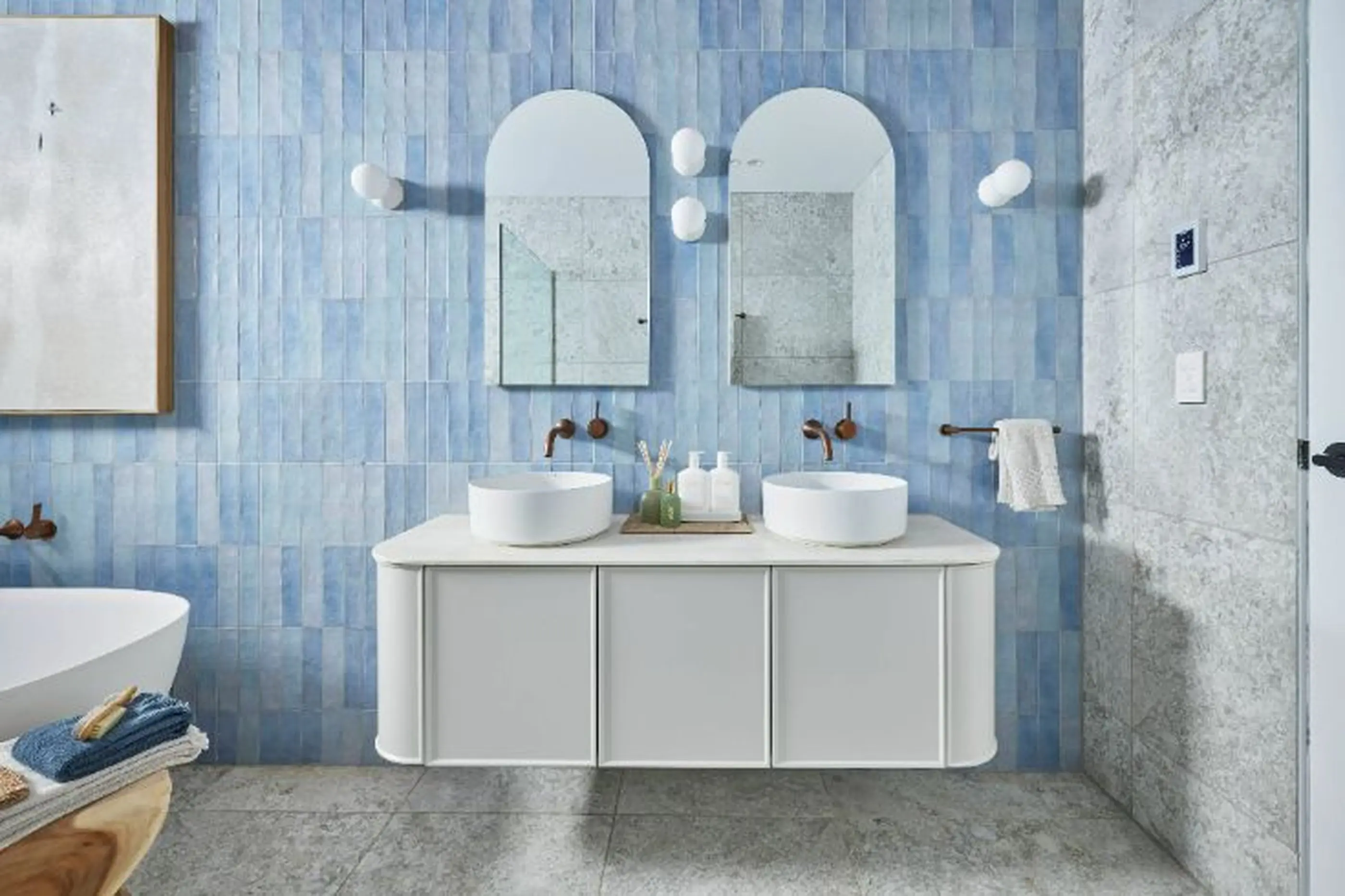 Modern bathroom with light blue tiled walls, white double vanity with vessel sinks, and arched mirrors with brass fixtures.