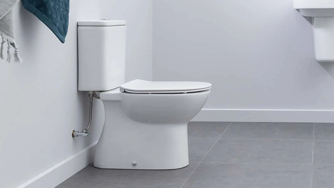 White toilet with closed lid in a minimalist bathroom with light gray walls and floor tiles, blue towel visible.