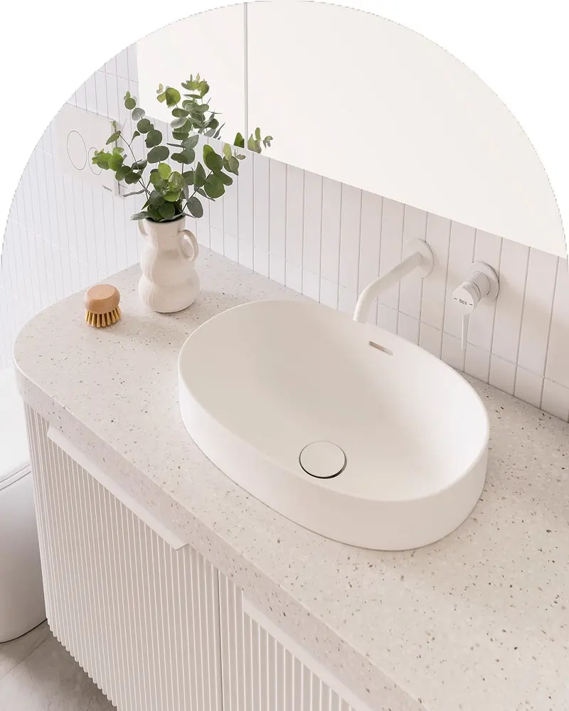 Modern white bathroom sink with terrazzo countertop, wall-mounted faucet, and eucalyptus plant in ceramic pitcher.