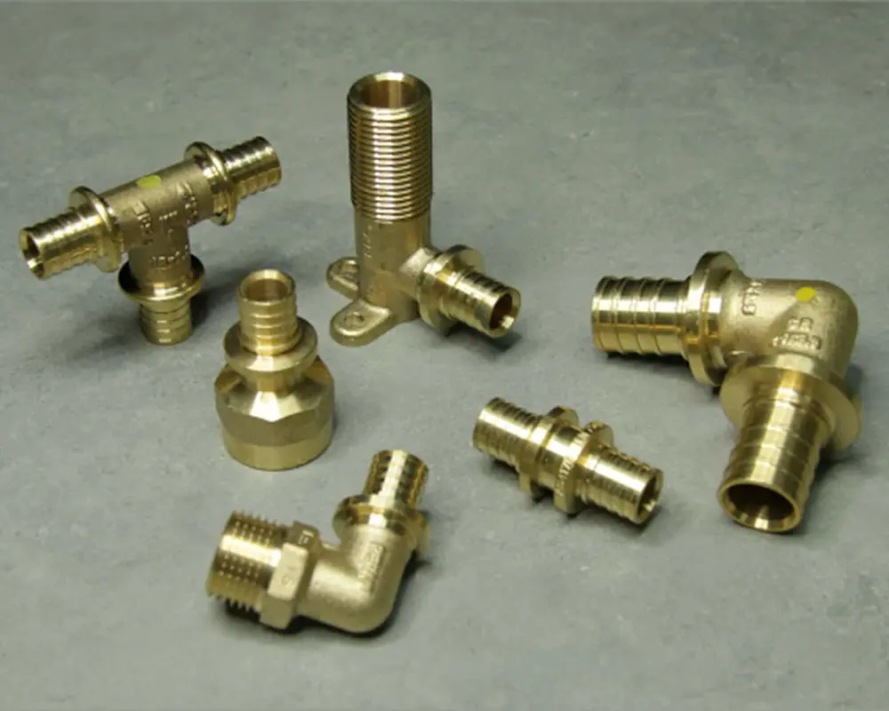 Various brass plumbing fittings including elbows, T-joints, and adapters arranged on a gray surface.