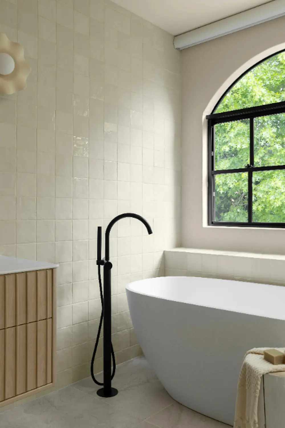 Modern bathroom with white freestanding tub, black floor-mounted faucet, cream tile walls, and arched window overlooking greenery.