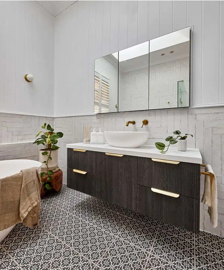 Modern bathroom with dark wood vanity, white vessel sink, patterned floor tiles, and potted plants on white paneled walls.