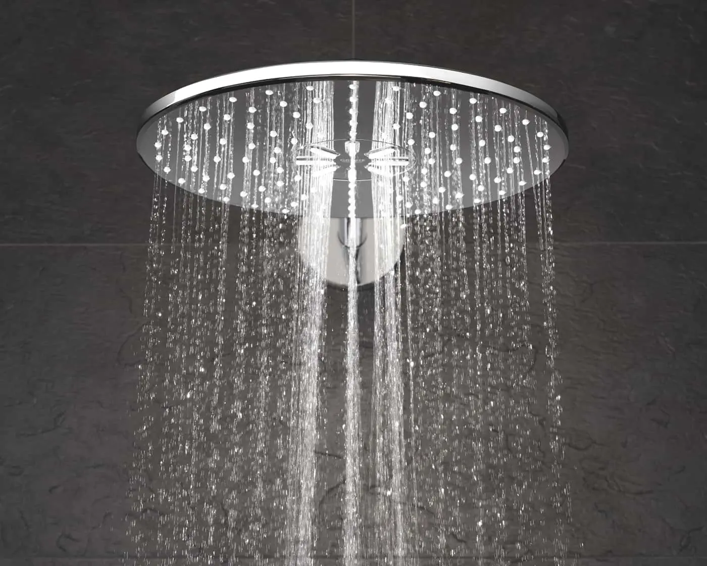 Modern circular rainfall shower head with water streaming down against dark tile background.