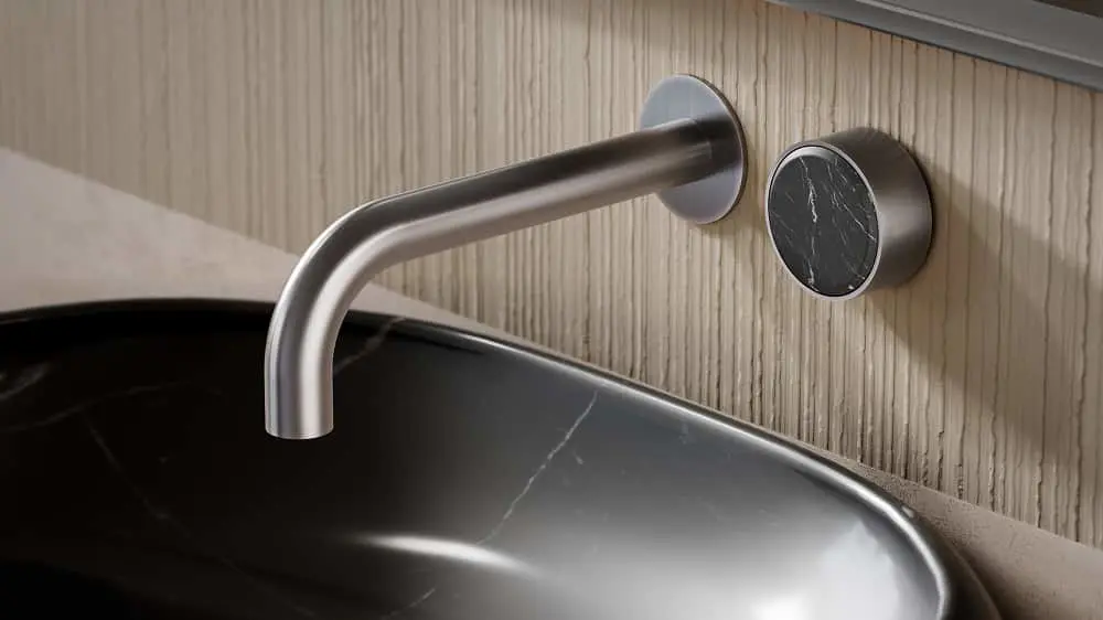 Modern bathroom sink with curved stainless steel wall-mounted faucet and black marble control knob on light wood wall.