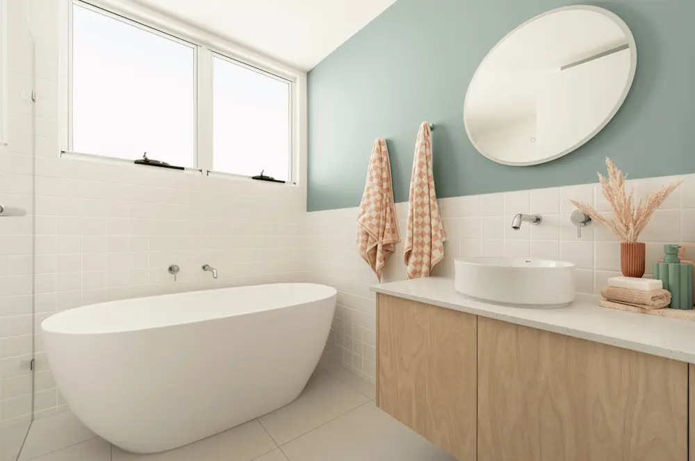 Modern bathroom with white freestanding tub, wooden vanity, round mirror, and mint green walls with peach accents.