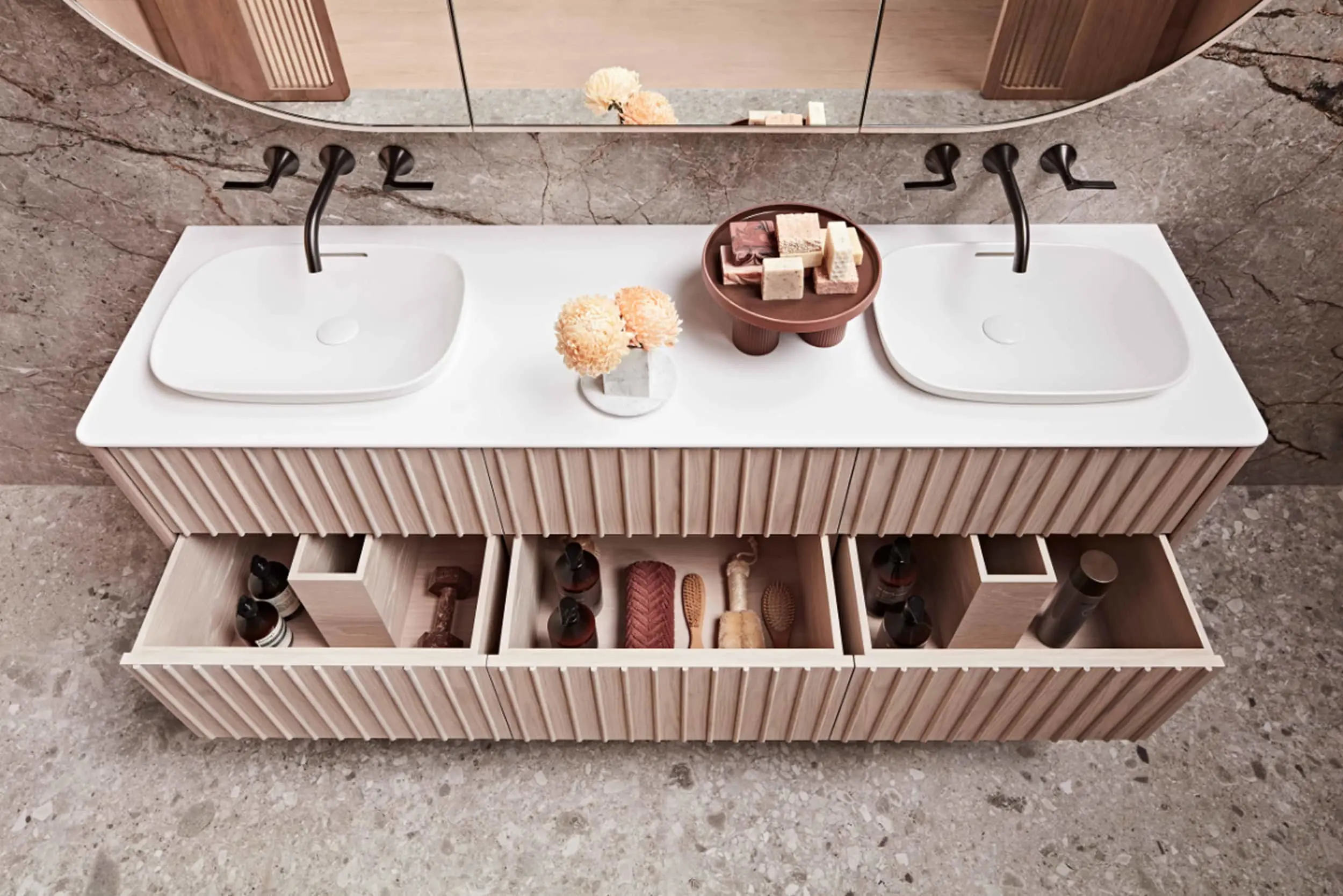 Modern bathroom vanity with dual white sinks, black faucets, open drawers showing organised toiletries, and decorative items on top.