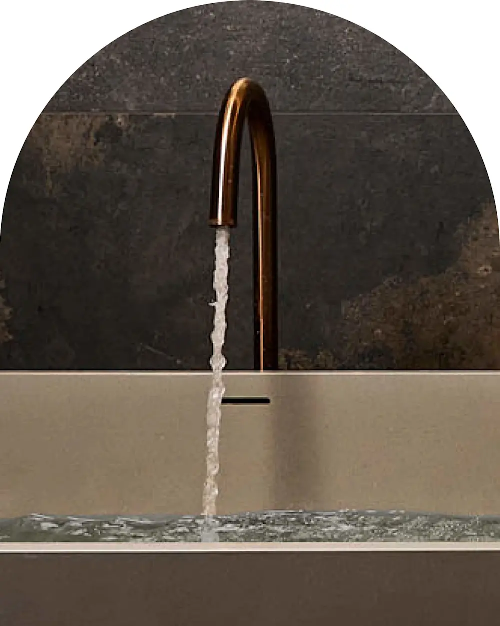 Copper faucet with running water against dark stone wall, flowing into a light-colored sink basin.