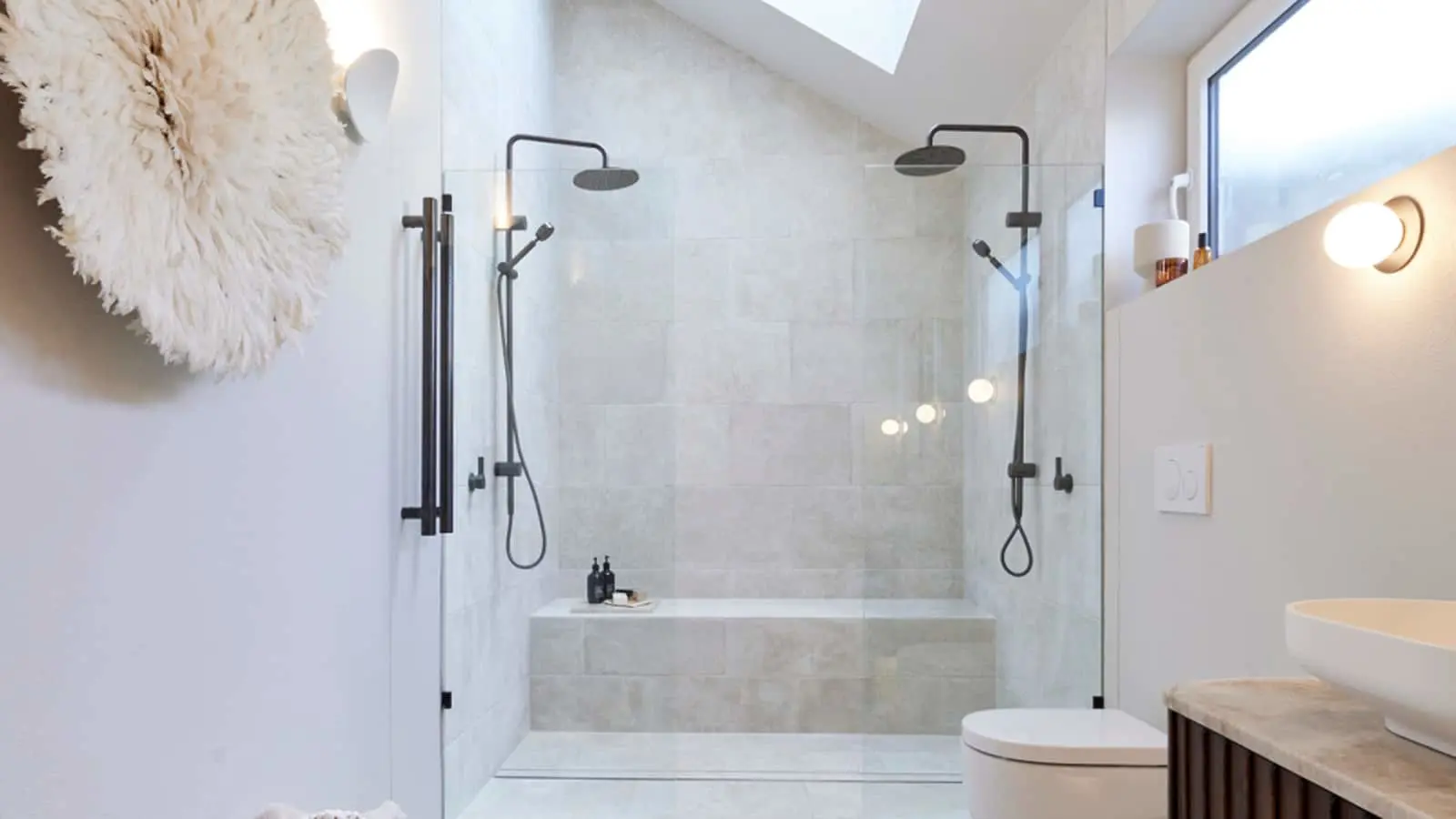 Modern bathroom with glass shower featuring dual black rainfall showerheads, light marble tiles, and a fluffy wall decoration.