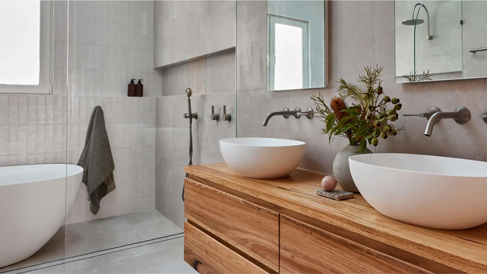 Modern bathroom with gray walls, wooden vanity with two white vessel sinks, bathtub, and arched mirror.