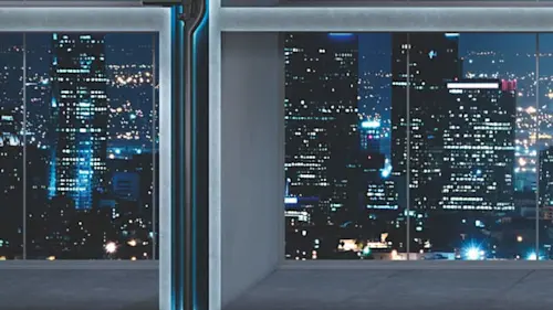 Night city skyline with illuminated skyscrapers viewed through large windows of an empty room.