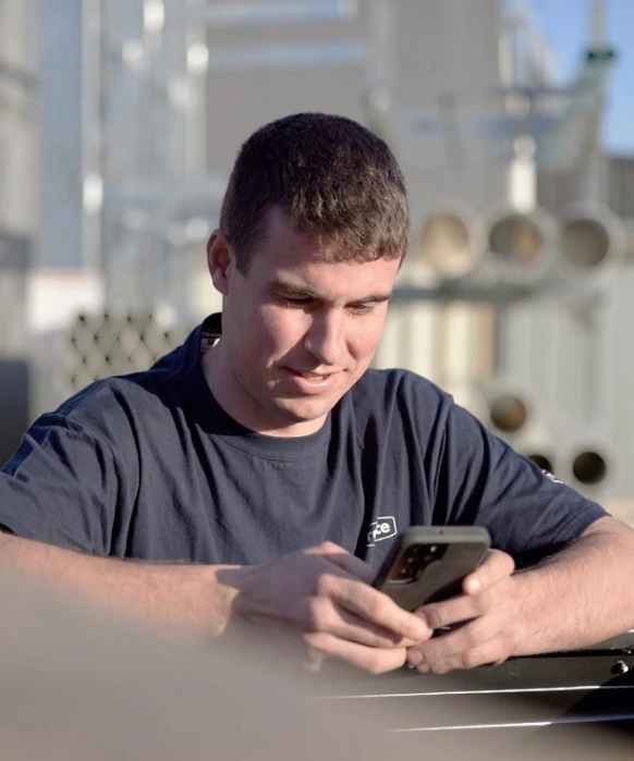Young man in navy blue t-shirt looking down at device, with blurred industrial background.
