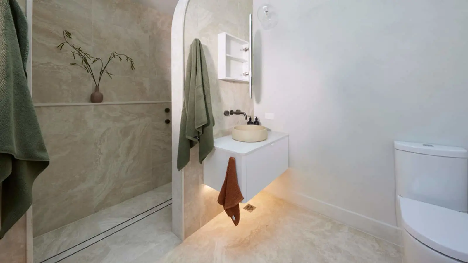 Modern bathroom with marble walls, white vanity, beige vessel sink, green towels, and minimalist design features.