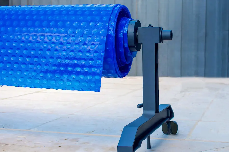 Blue bubble pool cover on a roller stand next to a swimming pool.