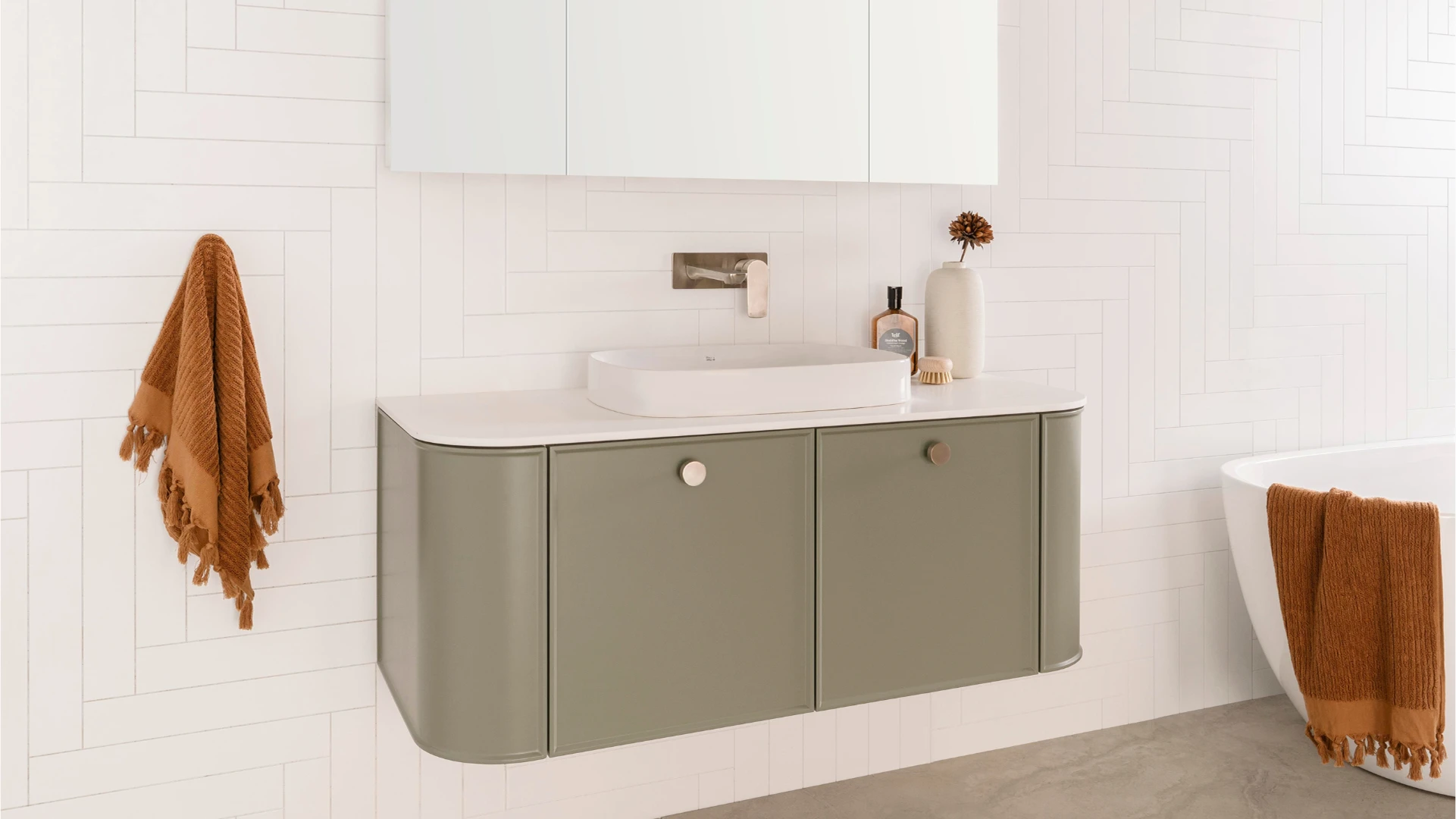 Modern bathroom with sage green floating vanity, white sink, and rust-colored towels against white tiled walls.
