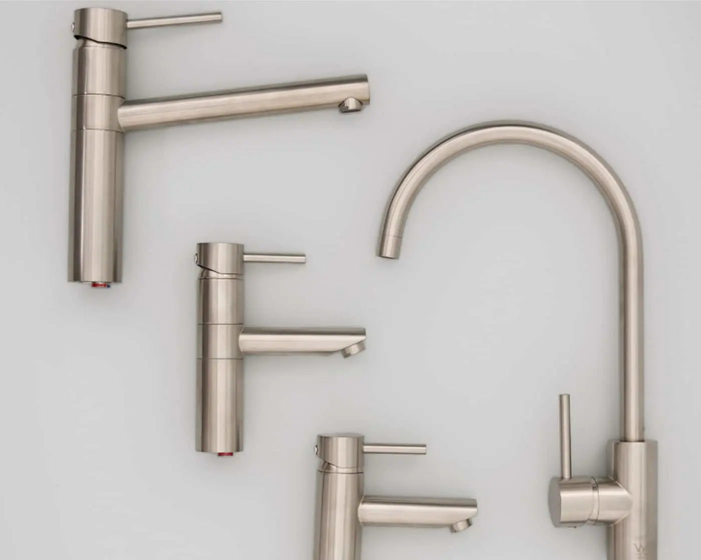 Four brushed nickel faucets arranged on a white surface, including three single-handle models and one tall gooseneck.