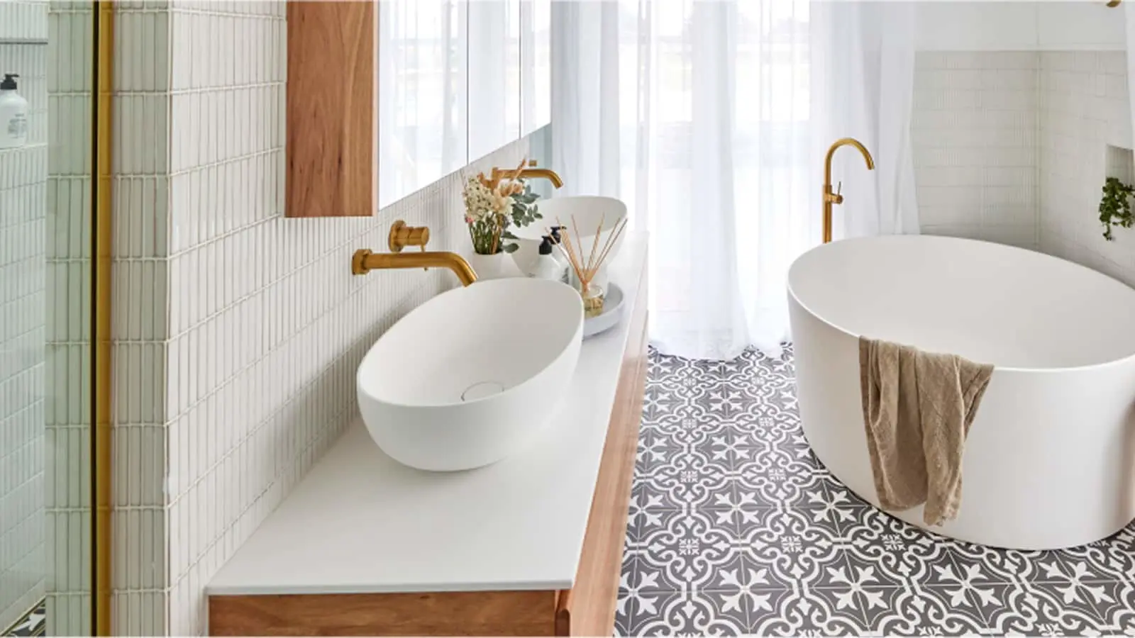 Modern bathroom with white oval sink, freestanding tub, gold fixtures, and patterned floor tiles.
