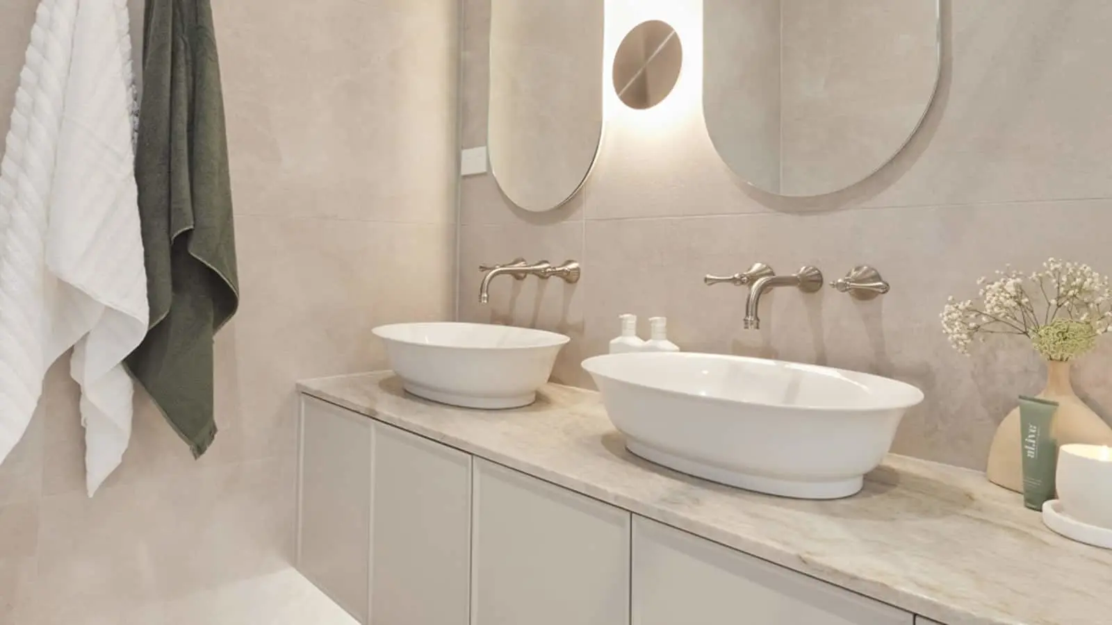 Modern bathroom with dual white vessel sinks, round mirrors, wall-mounted faucets, and hanging towels in white and green.