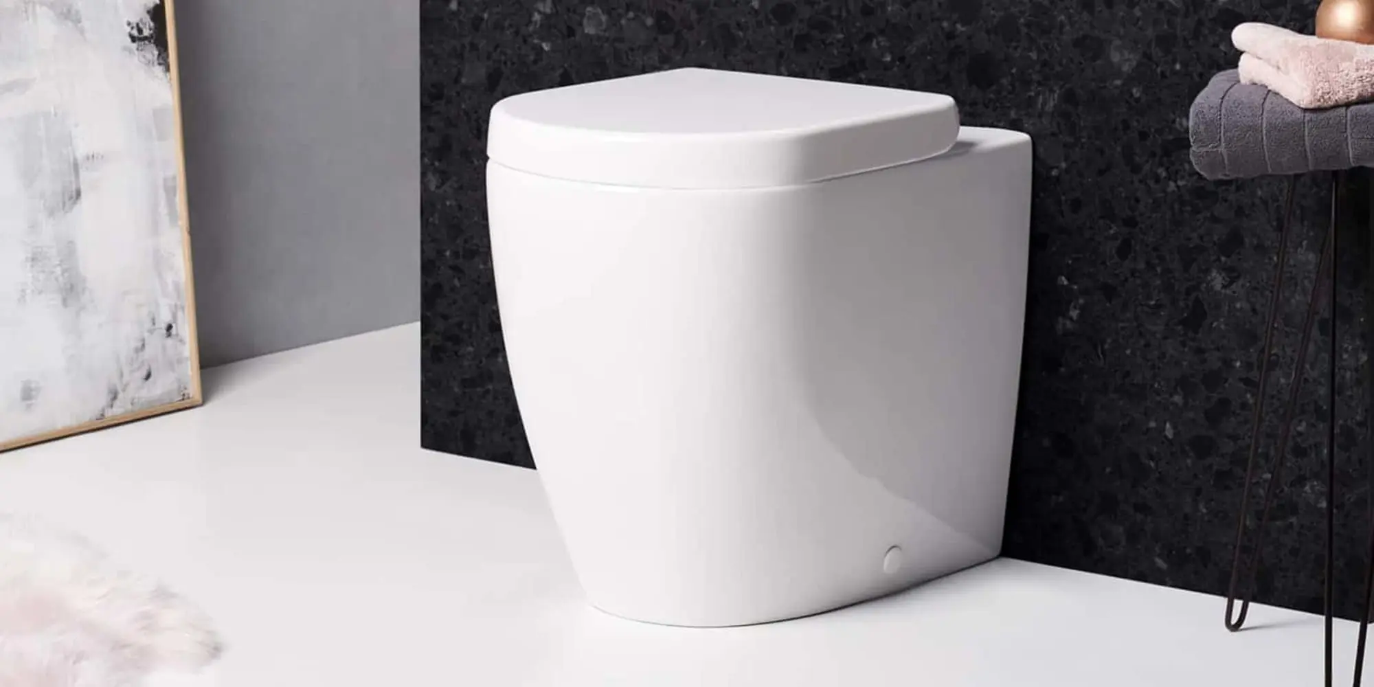 White square-shaped back-to-wall toilet with closed seat against a dark granite wall in a bathroom setting.