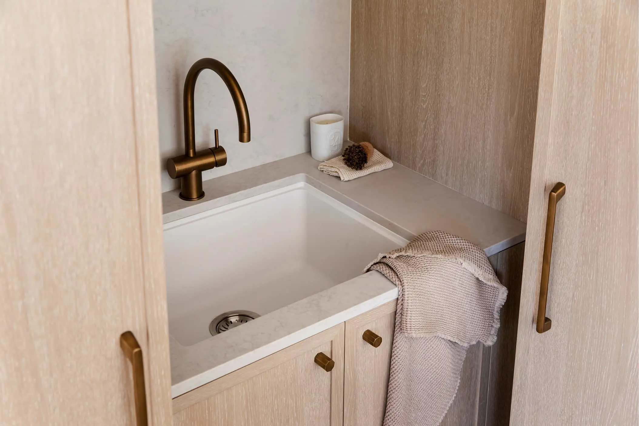 Modern kitchen sink with brass faucet, white basin, wooden cabinetry, and beige towel hanging on the side.
