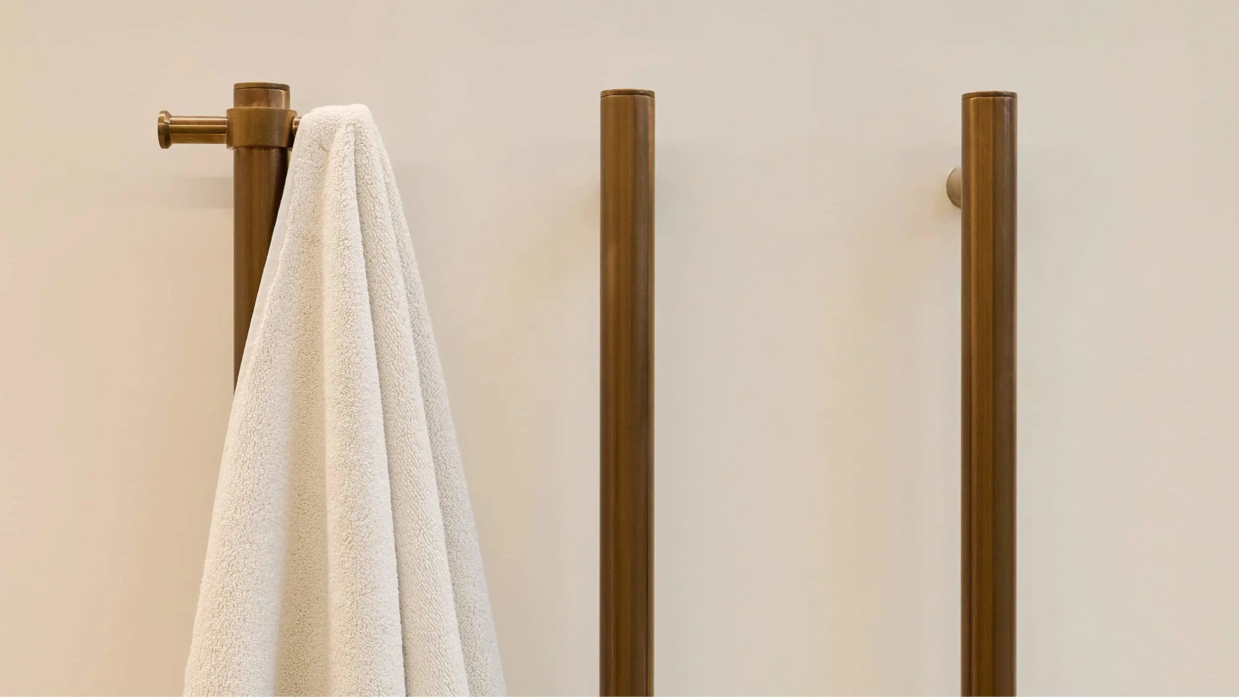 White towel hanging on brass bathroom fixture with two additional brass posts mounted on beige wall.