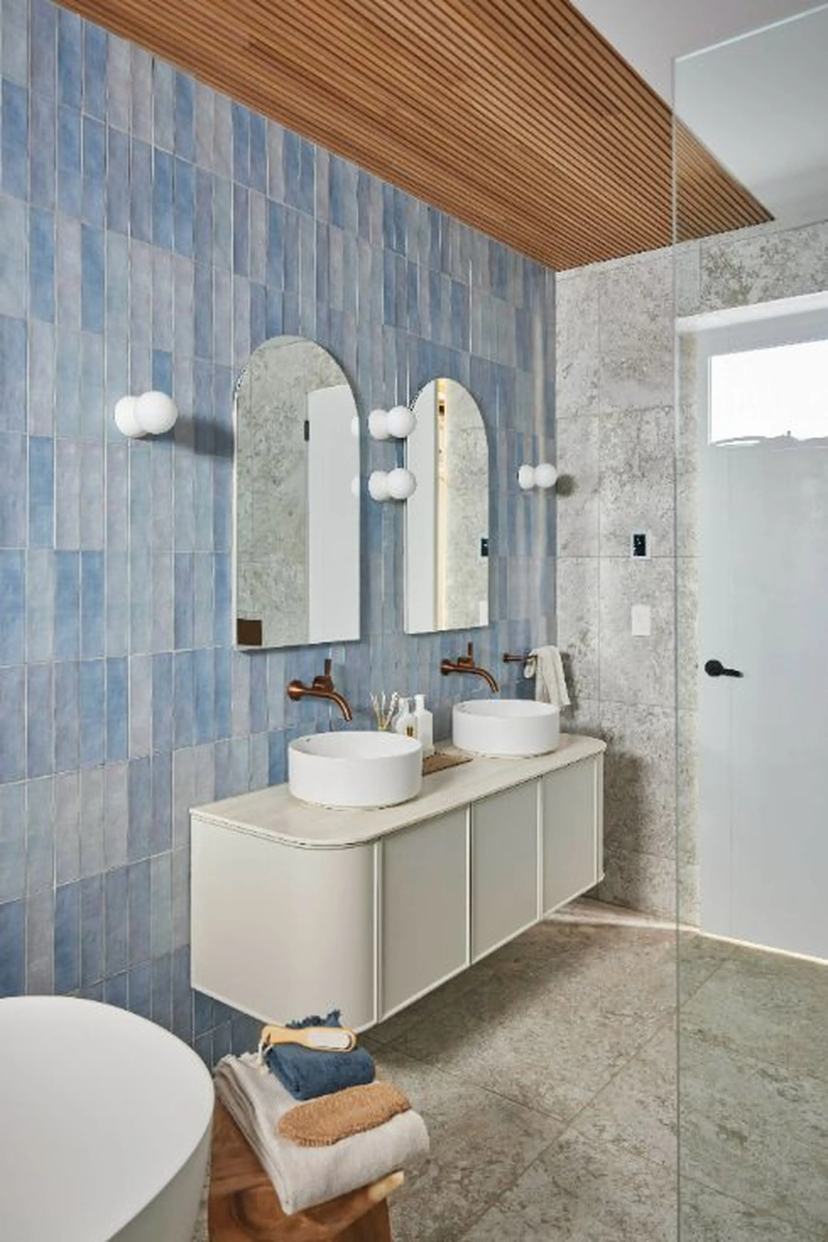 Modern bathroom with blue tile wall, white vanity with dual vessel sinks, wooden ceiling detail, and arched mirrors.