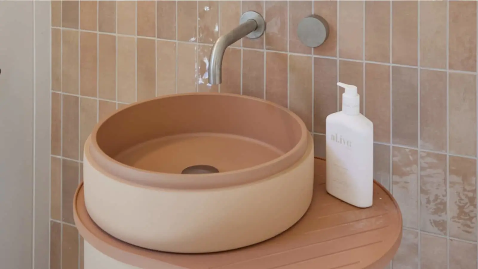 Terracotta circular sink on wooden counter with wall-mounted faucet and white soap dispenser against beige tiled wall.