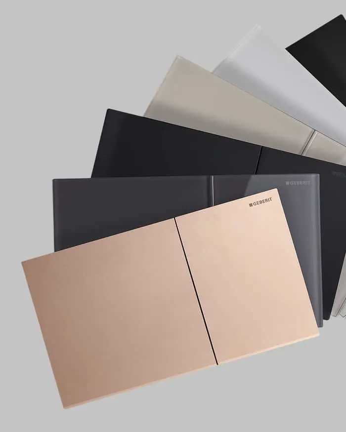 Overlapping Geberit flush plates in various colors including beige, dark gray, black, and white on a light background.