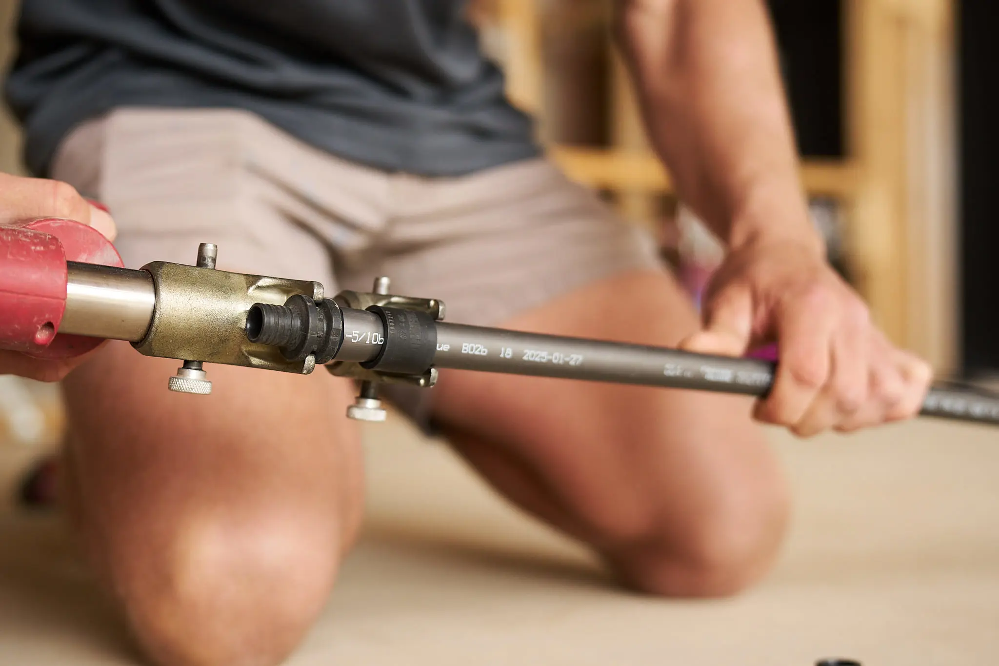 Person using a pipe fitting tool with brass connector and gray pipe marked with manufacturing date.
