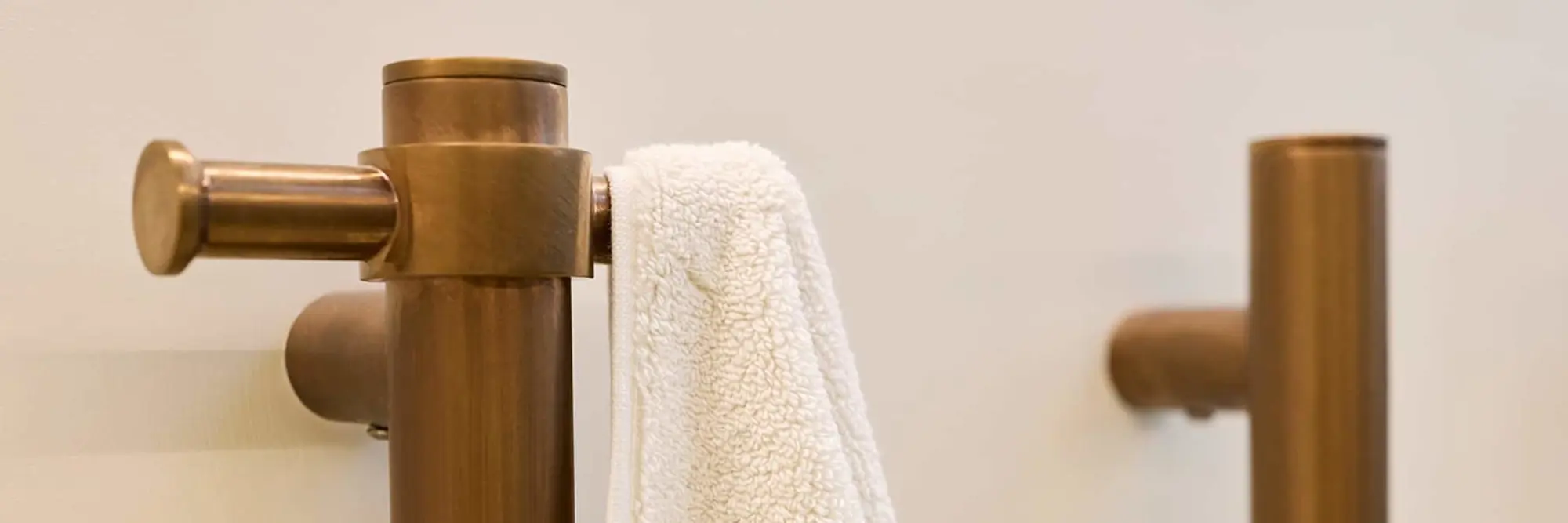 Brass bathroom fixtures with a white towel hanging on a towel bar against a cream-colored wall.