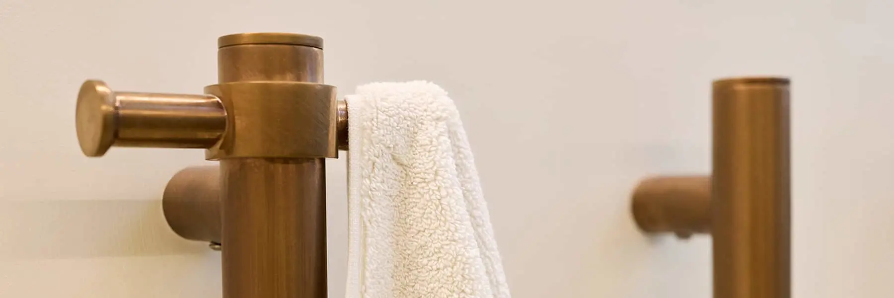 Brass bathroom fixtures with a white towel hanging on a towel bar against a cream-colored wall.