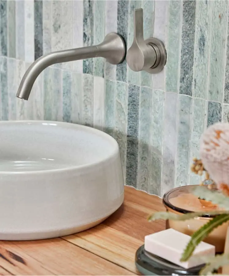 Modern bathroom sink with brushed nickel wall-mounted faucet, wooden countertop, and blue-green tile backsplash.