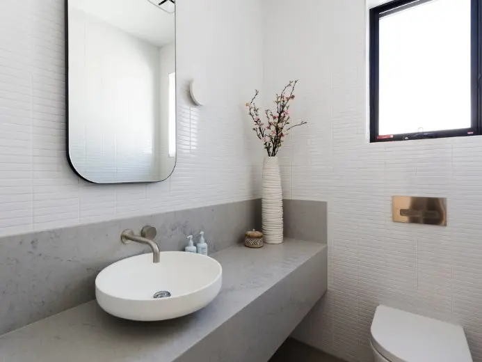 Modern bathroom with white oval sink, gray countertop, rounded mirror, and decorative vase with flowering branches.