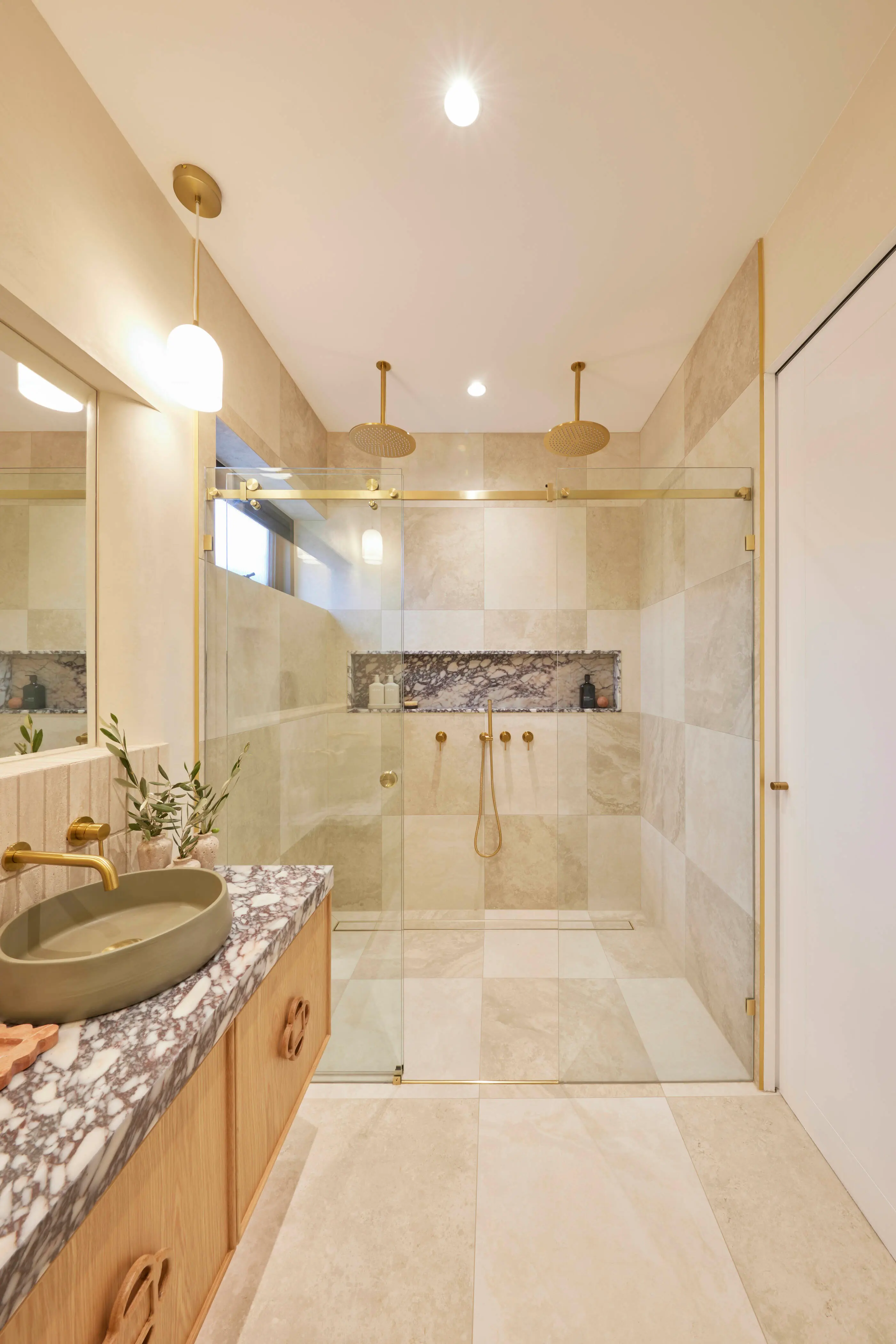 Modern bathroom with glass shower, beige tile walls, marble countertop, green sink, and gold fixtures.