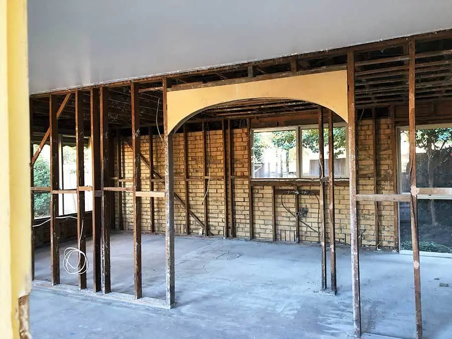 Interior of a home under renovation with exposed brick walls, wooden framing, and an arched doorway between rooms.