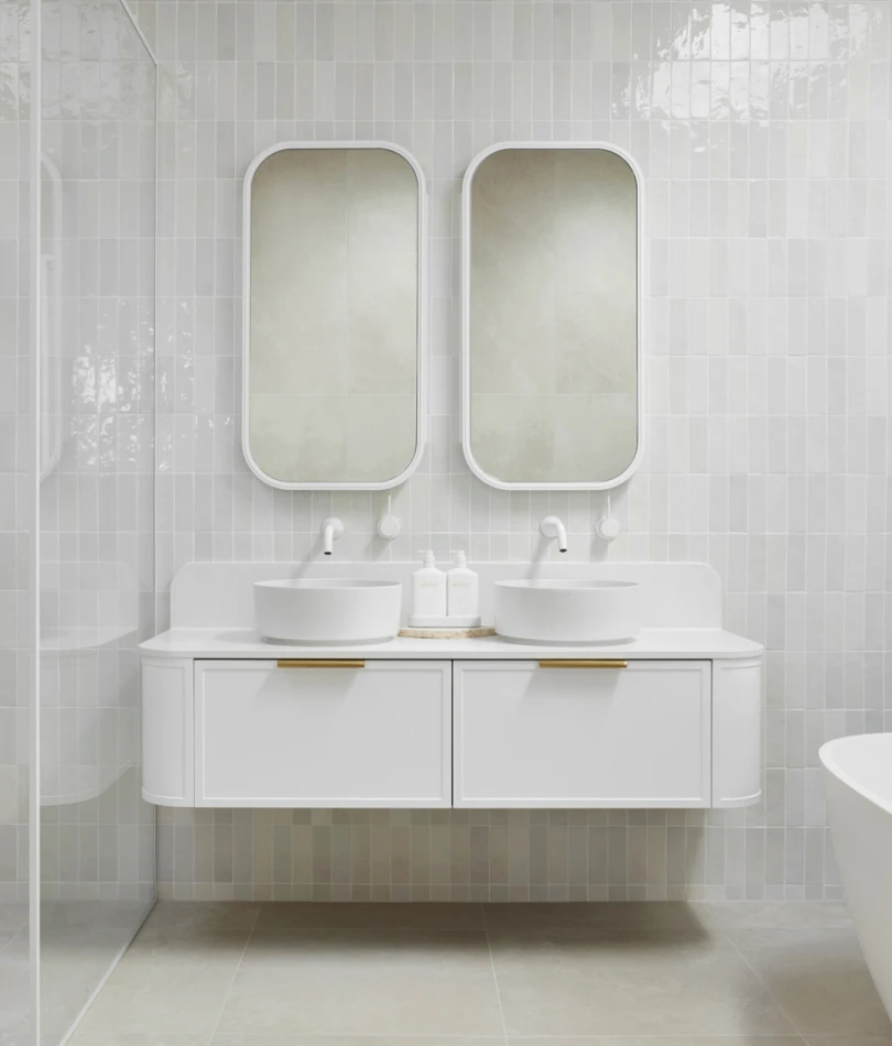Modern white bathroom with dual sinks, rounded mirrors, and floating vanity against light tile walls.