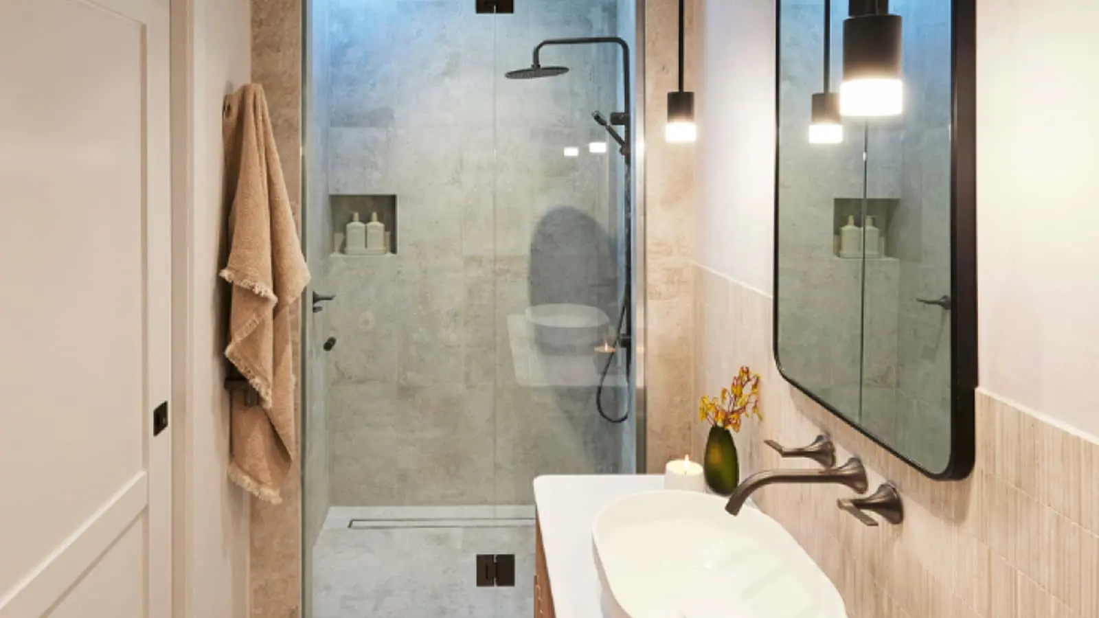 Modern bathroom with glass shower, marble tiles, white sink, hanging pendant lights, and a small green vase with flowers.