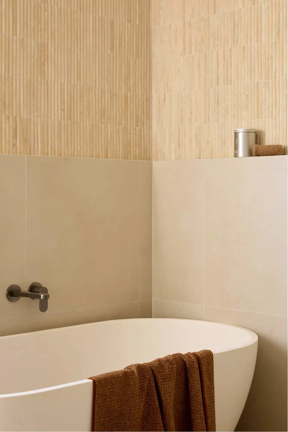 Modern bathroom with white freestanding tub, beige tile walls, accent wall, and gunmetal fixtures.